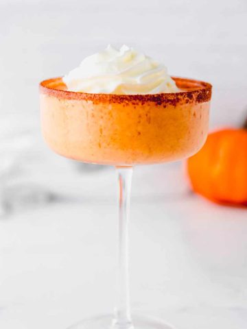 Close view of a pumpkin cocktail in a coupe glass rimmed with cinnamon and sugar.