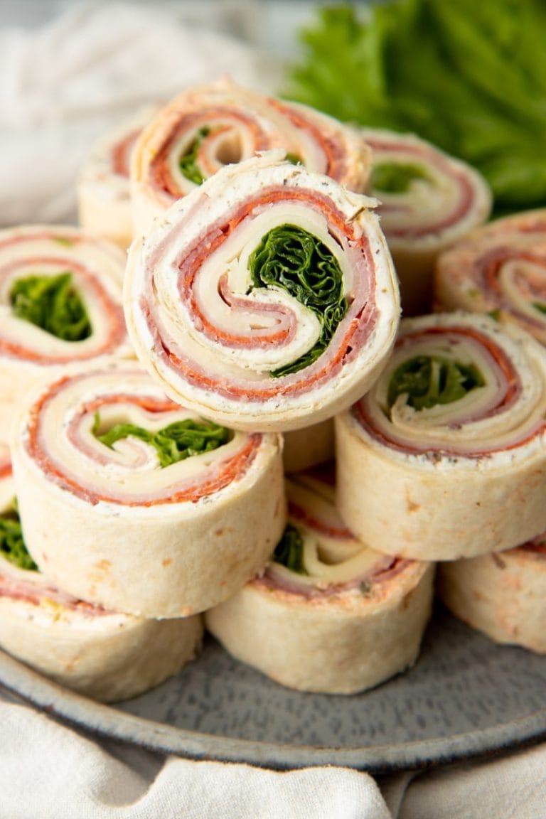 Serving platter of pinwheel appetizers stacked with one on top showing all the spiraled layers inside.