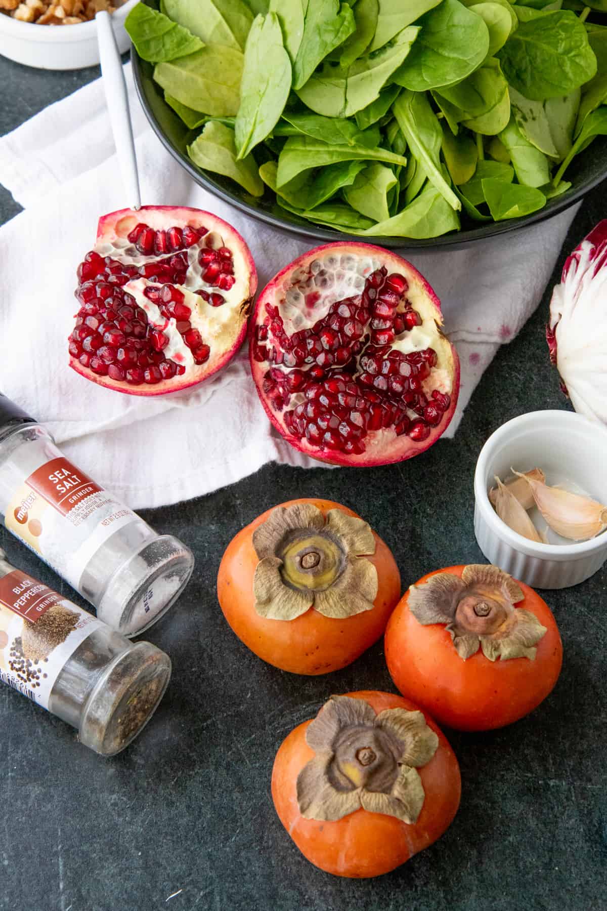 Persimmons, pomegranates, and spinach sit next to salt, pepper, and garlic.