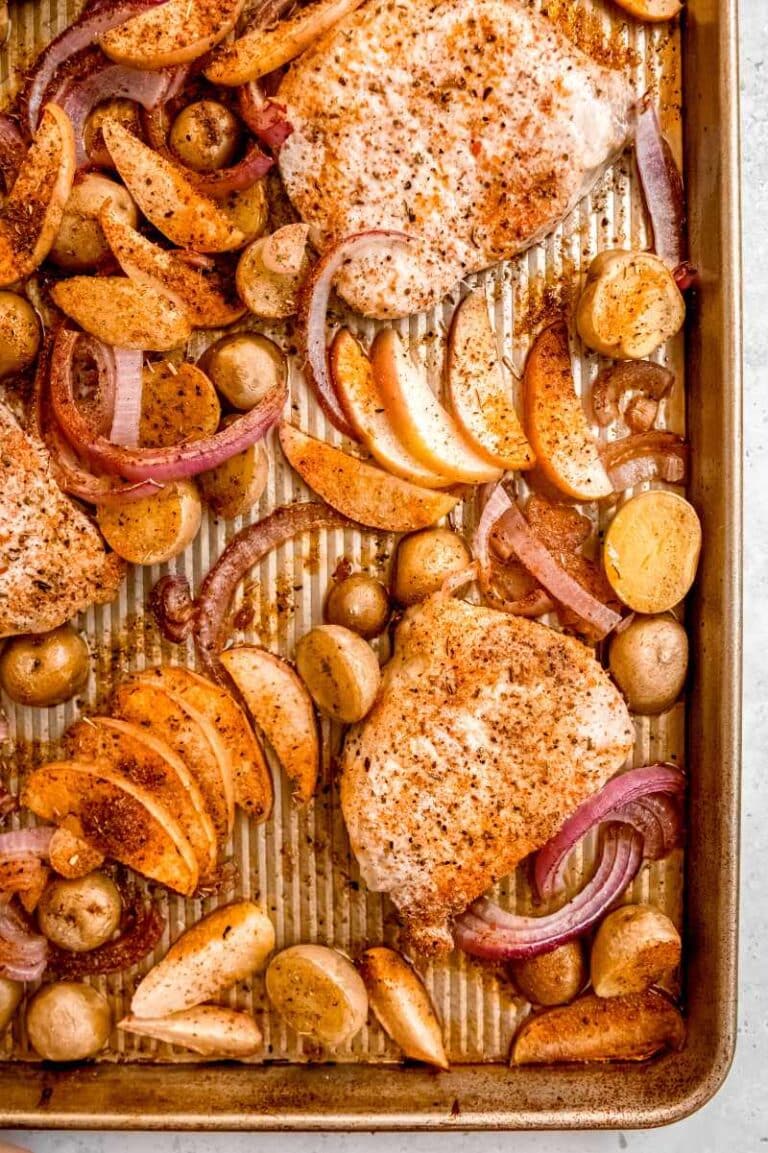 Overhead of pork chop dinner in a baking pan with seasoned chops, potatoes, and apple slices.