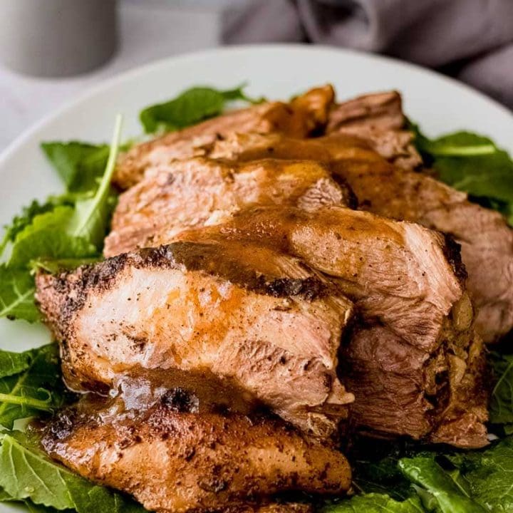 Close up of sliced and plated pork roast topped with gravy.