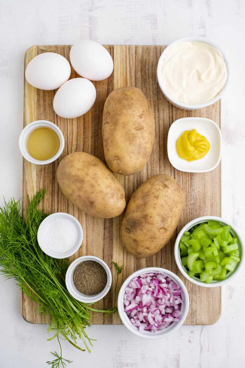 Overhead of all ingredients needed to prepare a flavorful potato salad, including russet potatoes, celery, red onion, and mayonnaise.