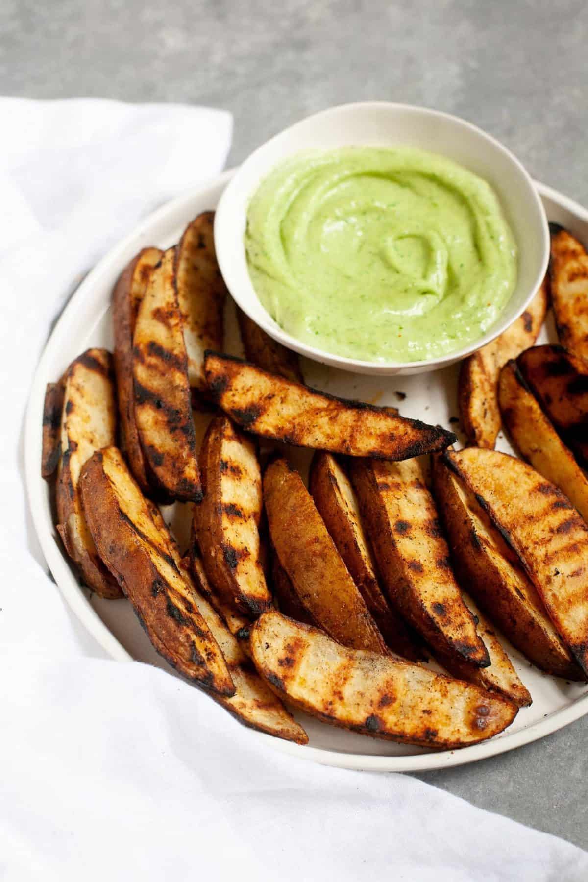 Side angle shot of Perfect Grilled Potato Wedges with a small dish of sauce