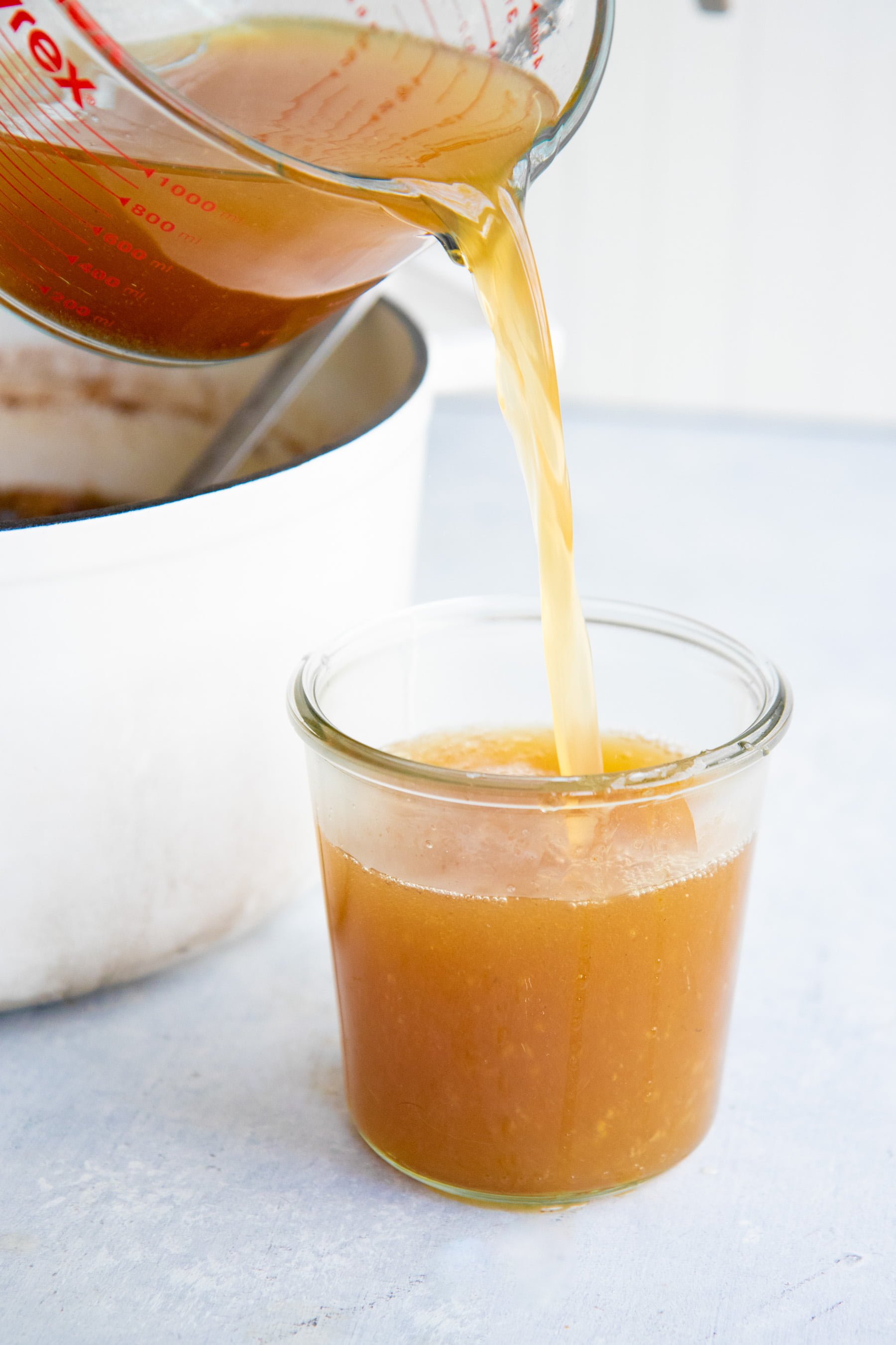 Glass Pyrex measuring cup pouring bone broth into a glass jar