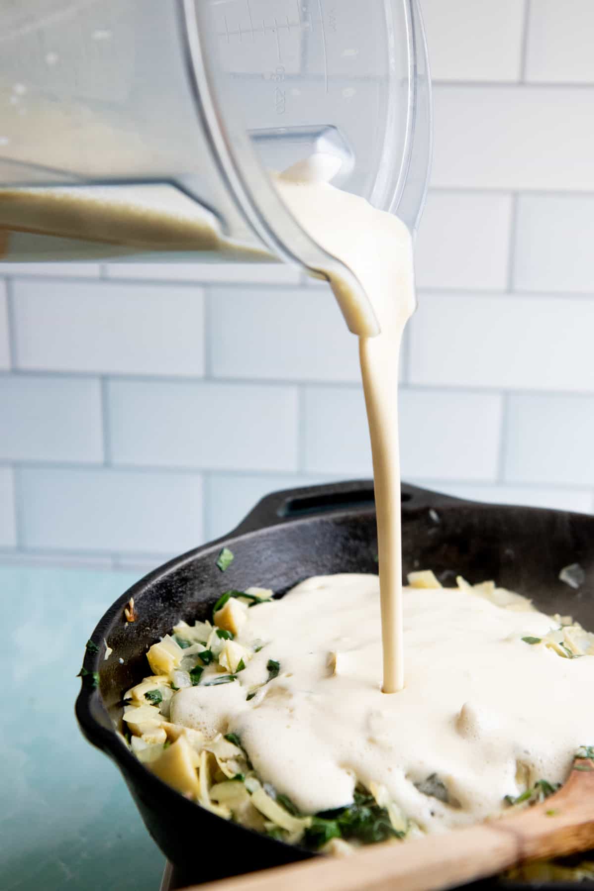 Cashew cream gets poured over a skillet of artichoke hearts and spinach.