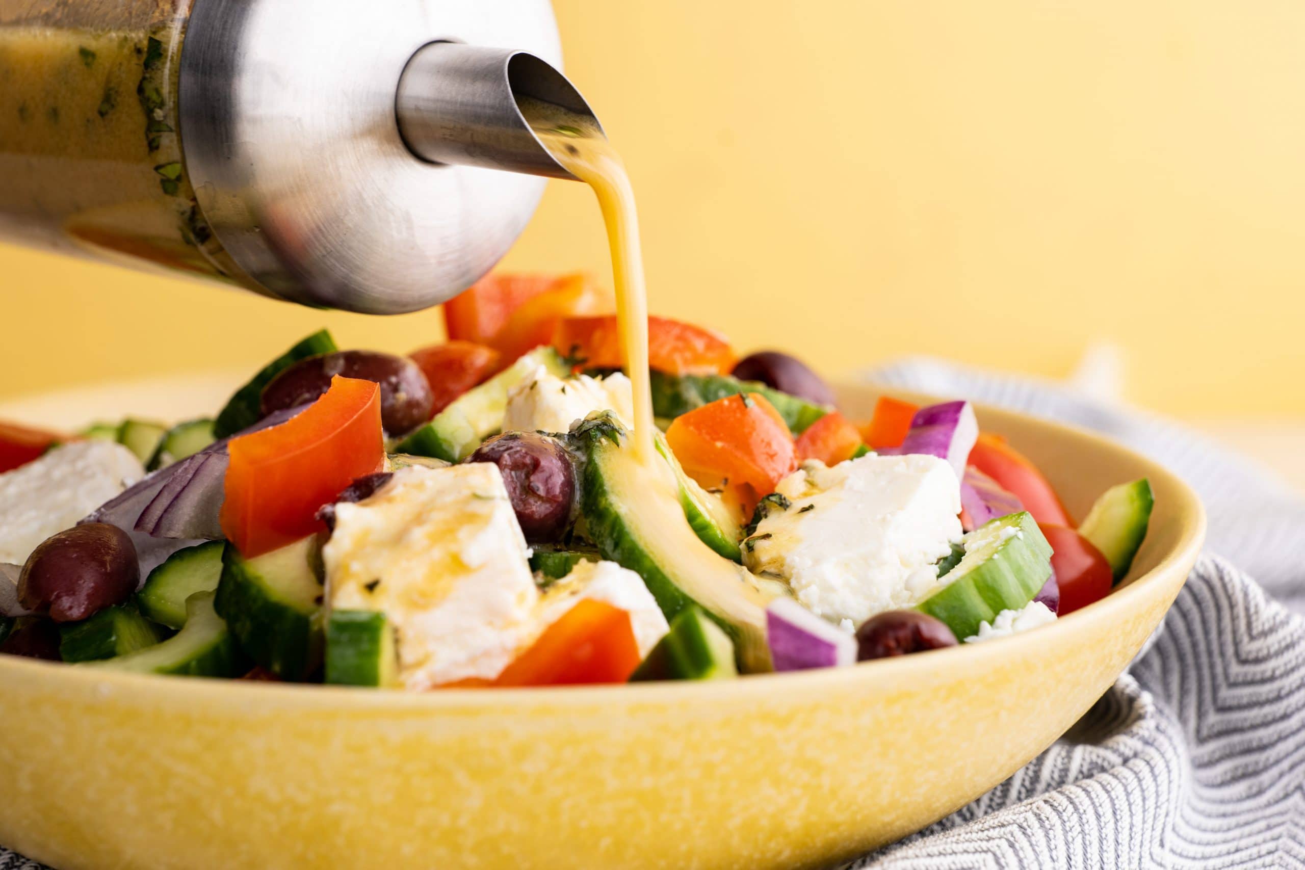 Close view of pouring homemade lemon vinaigrette on a fresh greek salad.