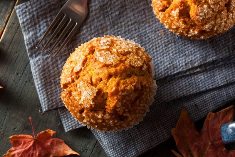 Top view of a bakery-style pumpkin muffin with autumn leaves around it.