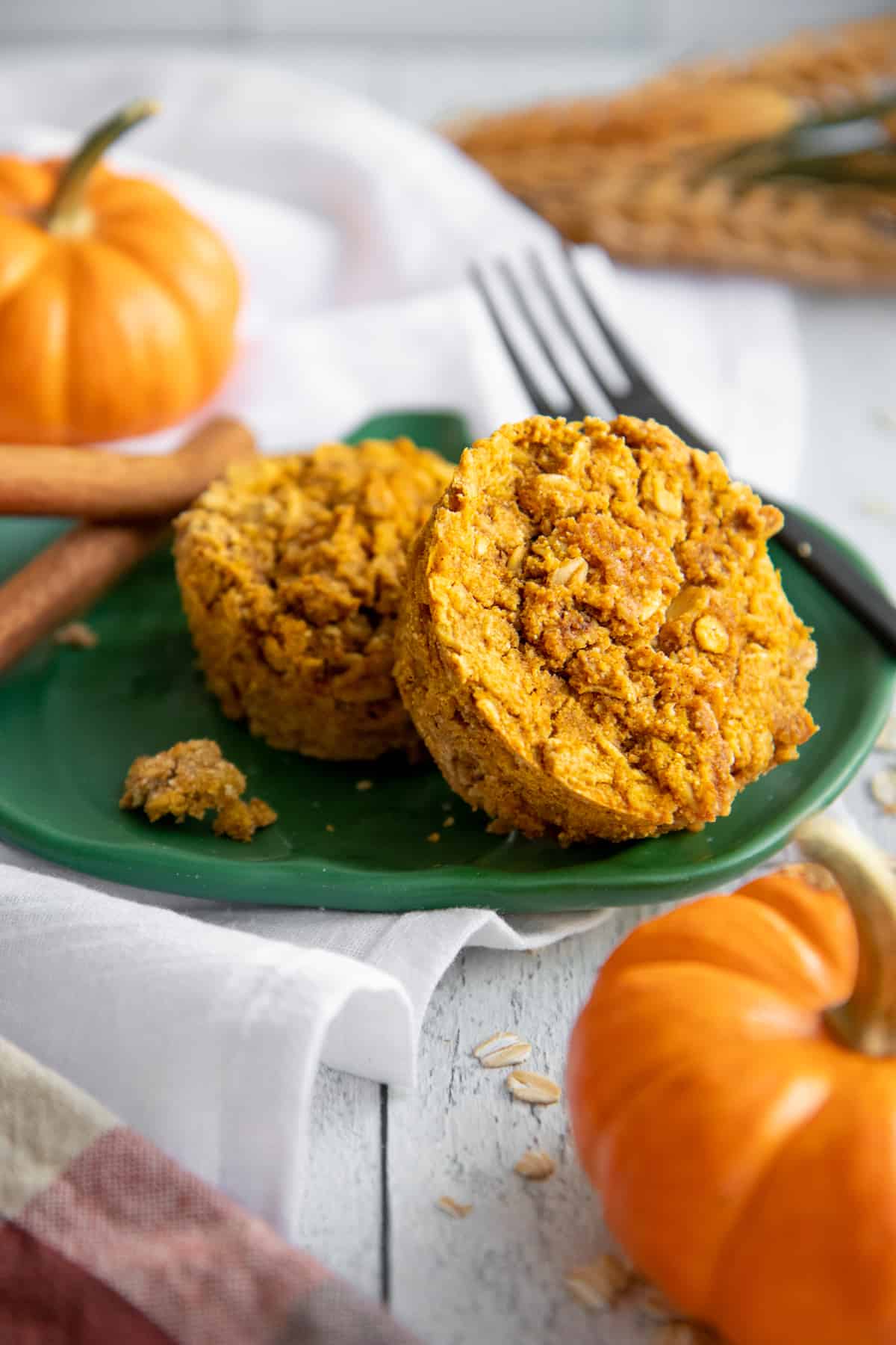 Two Pumpkin Spice Baked Oatmeal Cups on a green plate, with mini pumpkins nearby