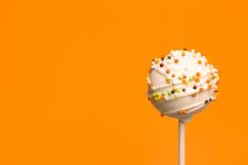 A cake pop covered with white candy melt and Halloween sprinkles.