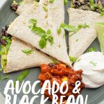 Quesadilla triangles on a gray plate, with a mound of salsa and a mound of sour cream next to them. A text overlay reads "Avocado and Black Bean Quesadillas."