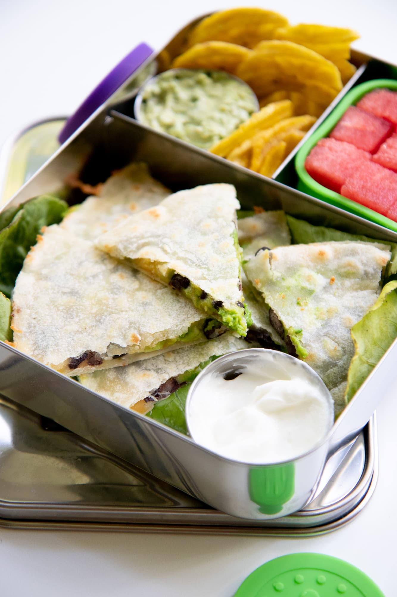 Stainless steel divided lunchbox with quesadilla, watermelon, plantain chips, and guacamole