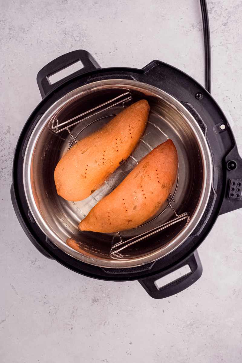 Two raw sweet potatoes in an instant pot on the steamer rack set over water.