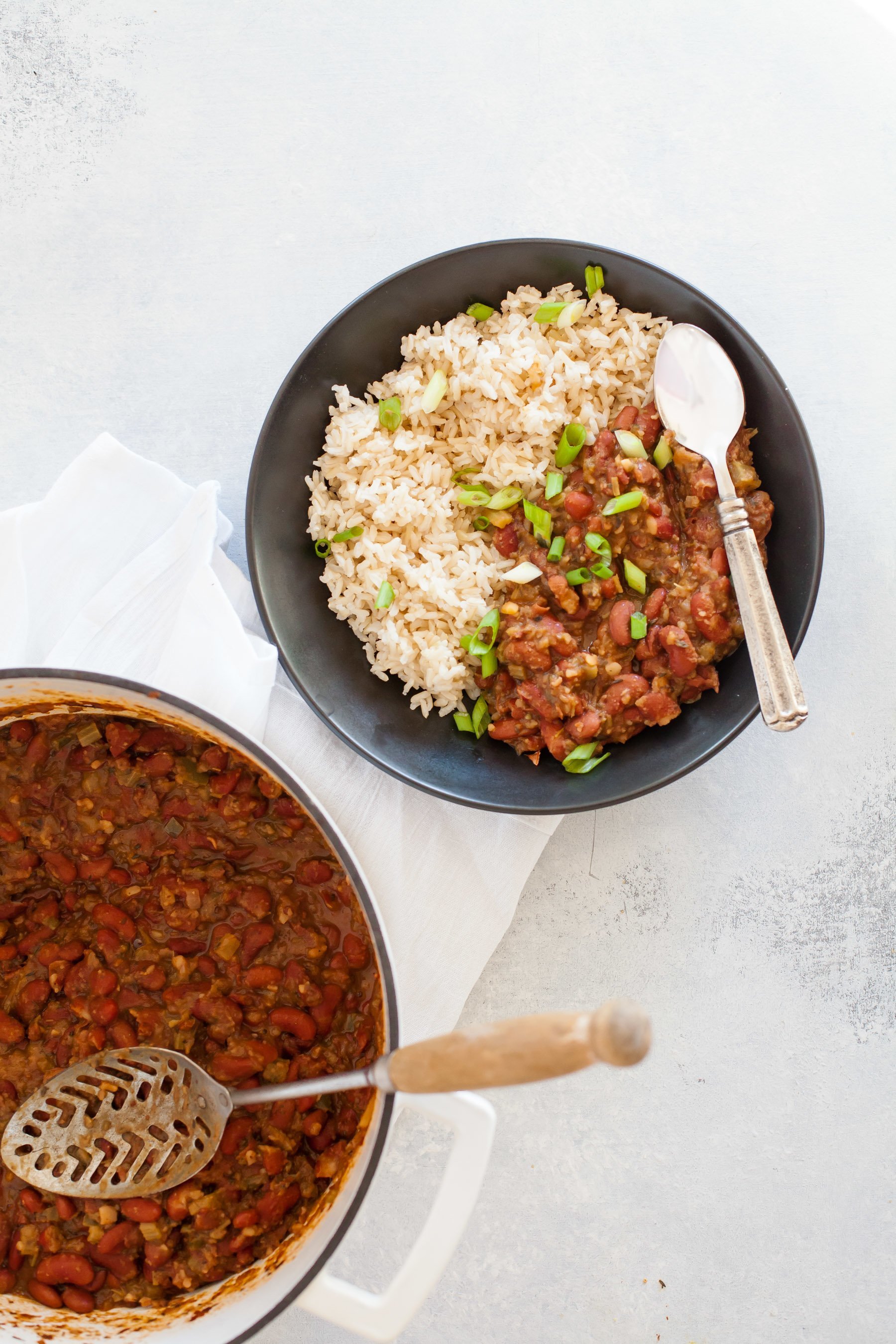 Gray bowl full of Vegan Red Beans and Rice with a spoon, next to a pot of beans