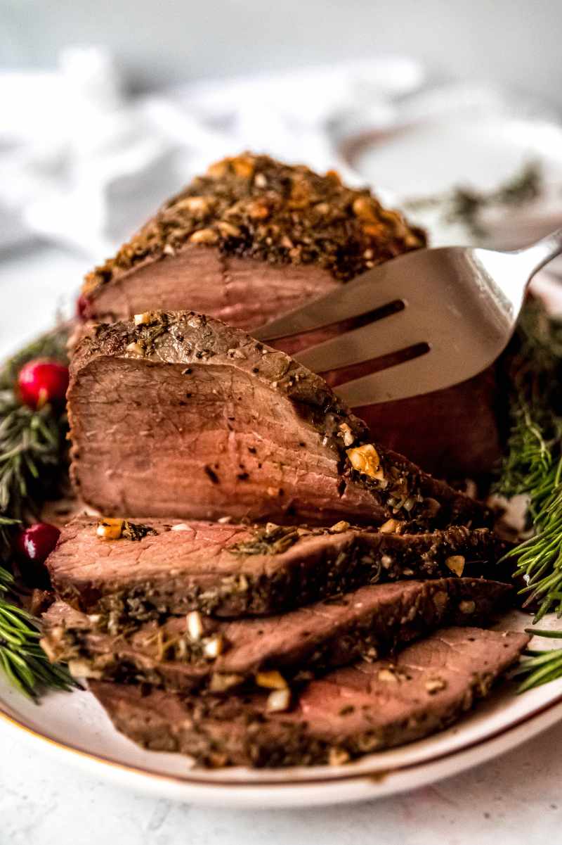 A large serving fork lifts a slice of roast beef from an oval platter.