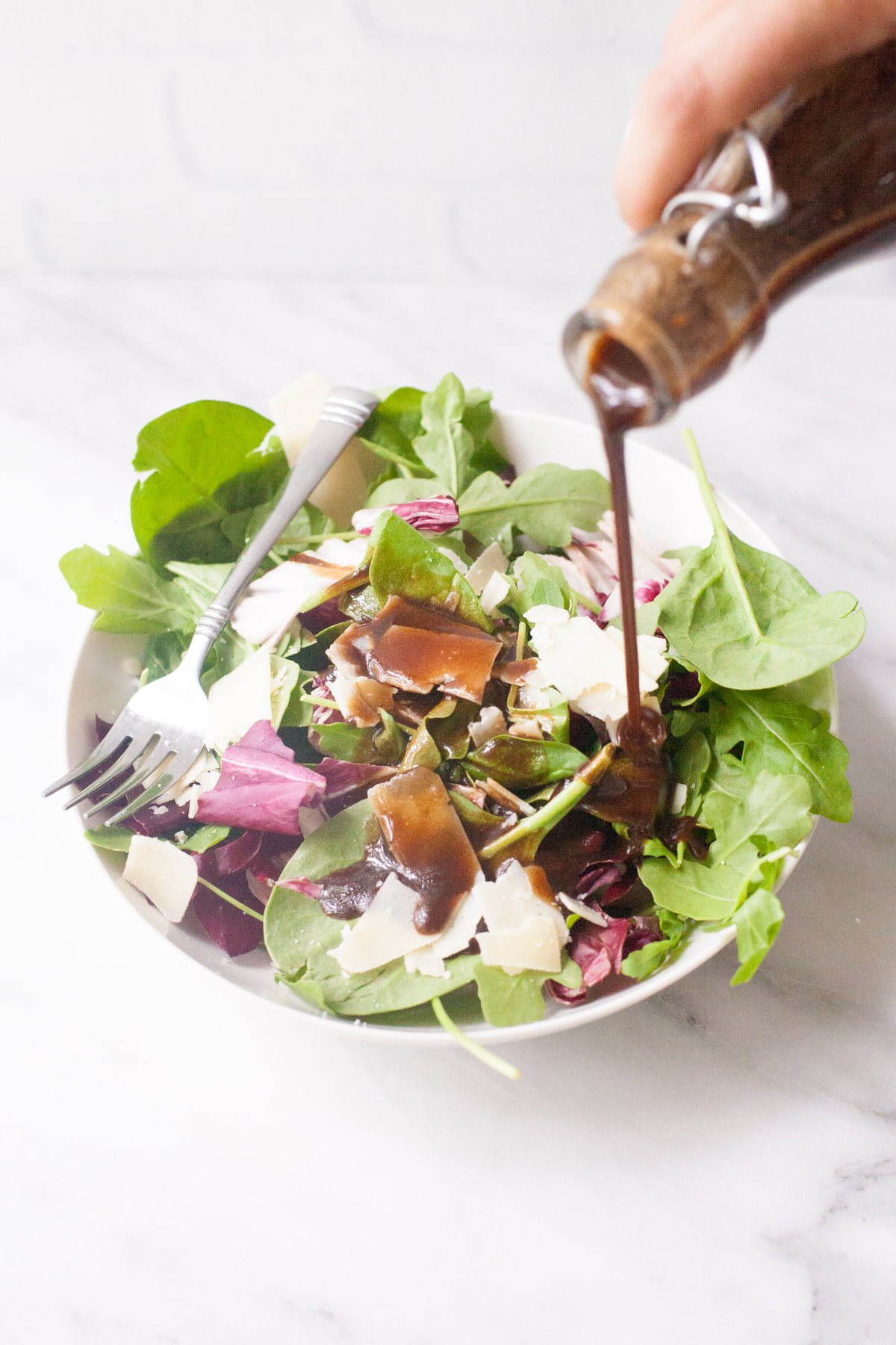 A hand pours homemade balsamic vinaigrette over a side salad.