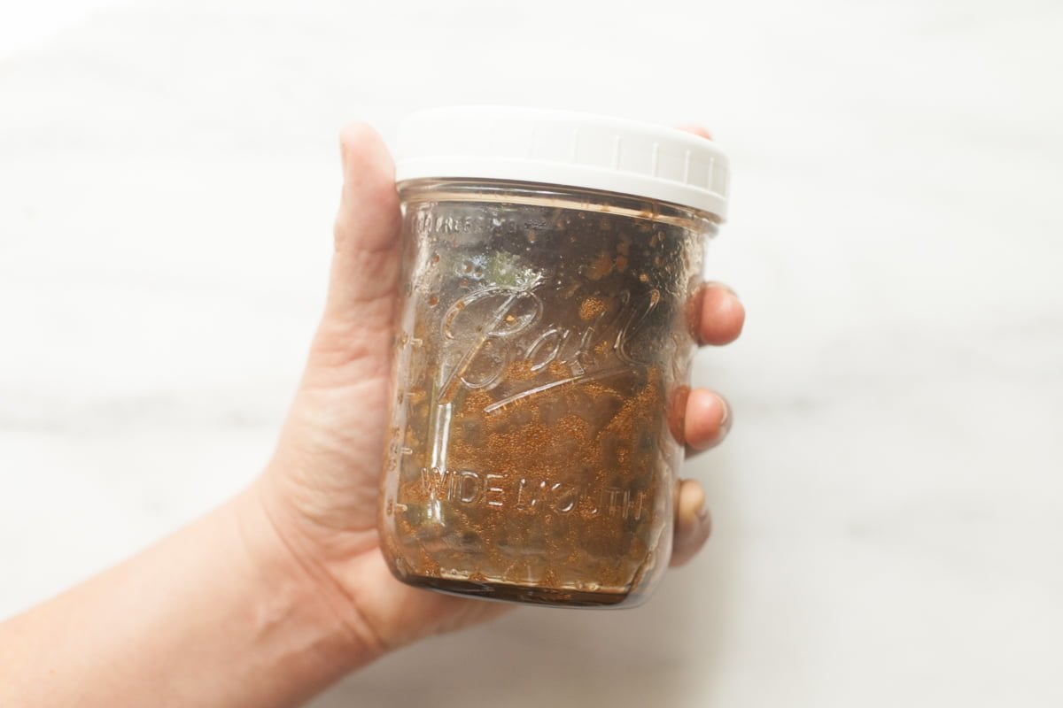 A hand holds out a half pint mason jar filled with balsamic vinaigrette