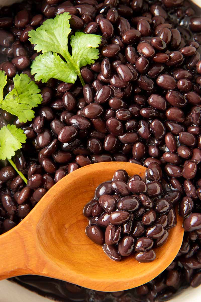 Close up of a wooden spoon scooping cooked black beans.