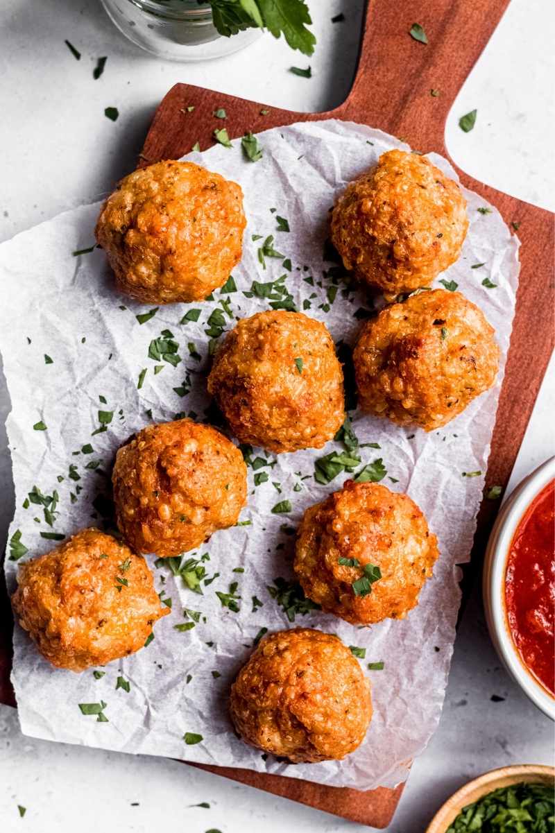 Finished chicken meatballs on a serving board, garnished with chopped fresh herbs with dipping sauce on the side.