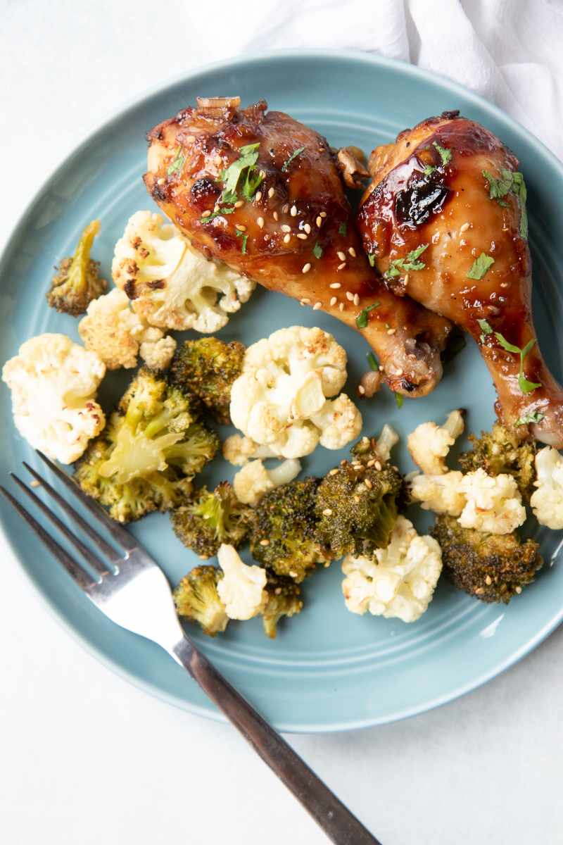 Roasted veggies beside baked chicken on a teal plate with a fork.