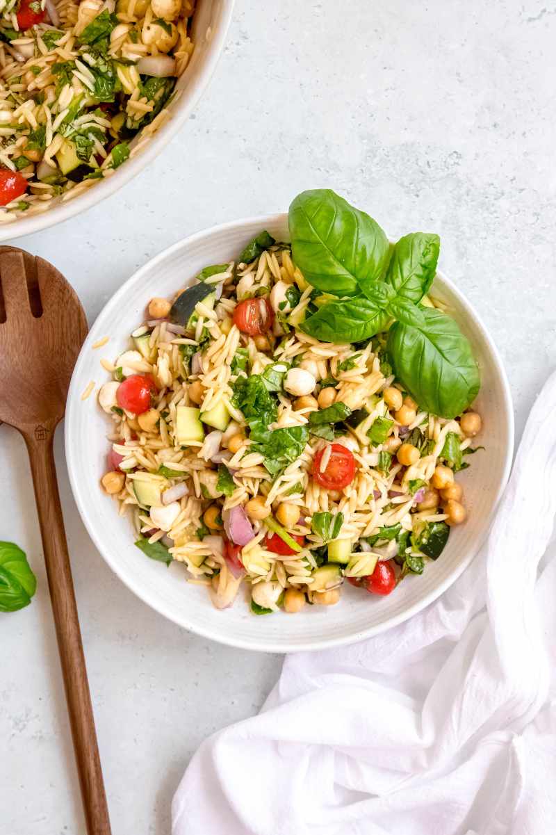 A white serving bowl of pasta salad garnished with fresh basil on a light background.