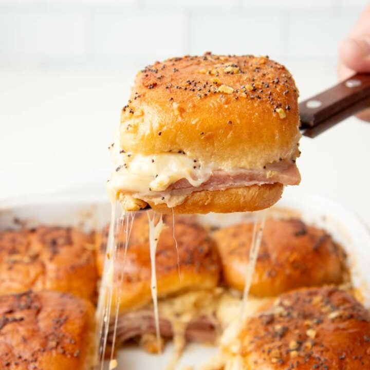 A spatula serves up a baked slider from the center of a pan of other sliders.