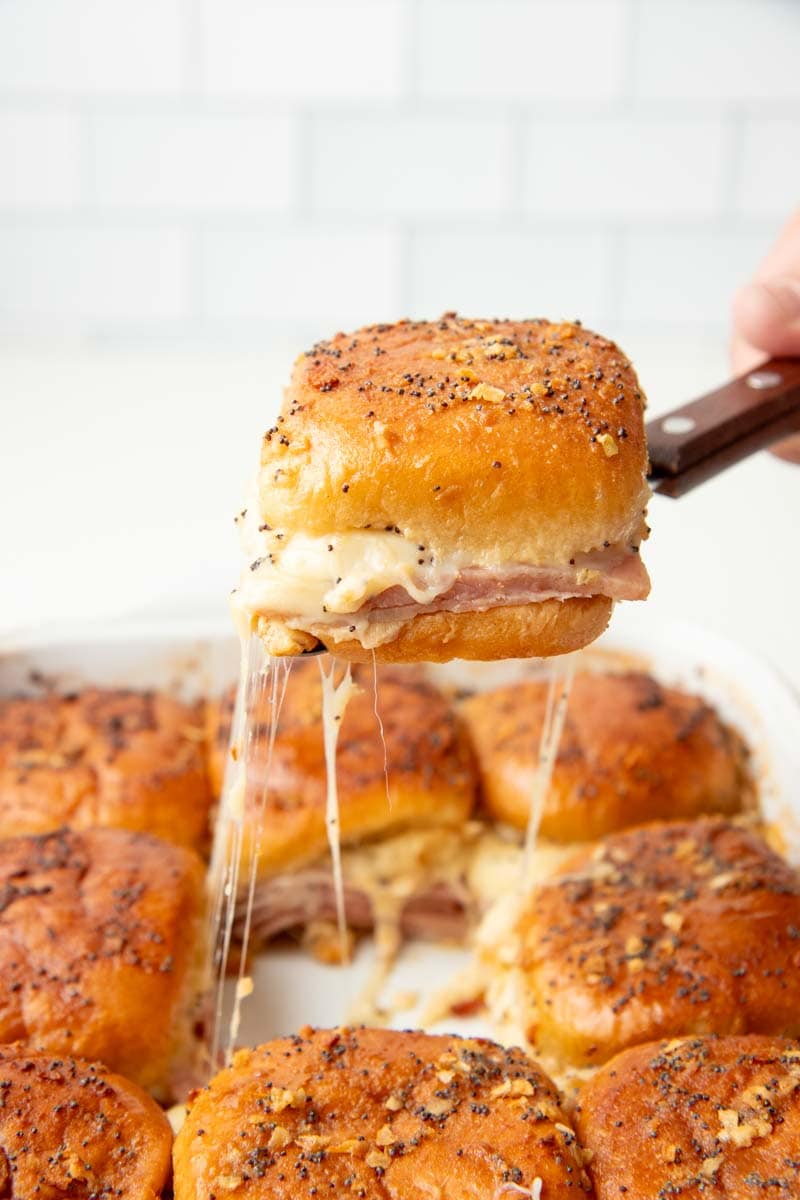 A spatula serves up a baked slider from the center of a pan of other sliders.