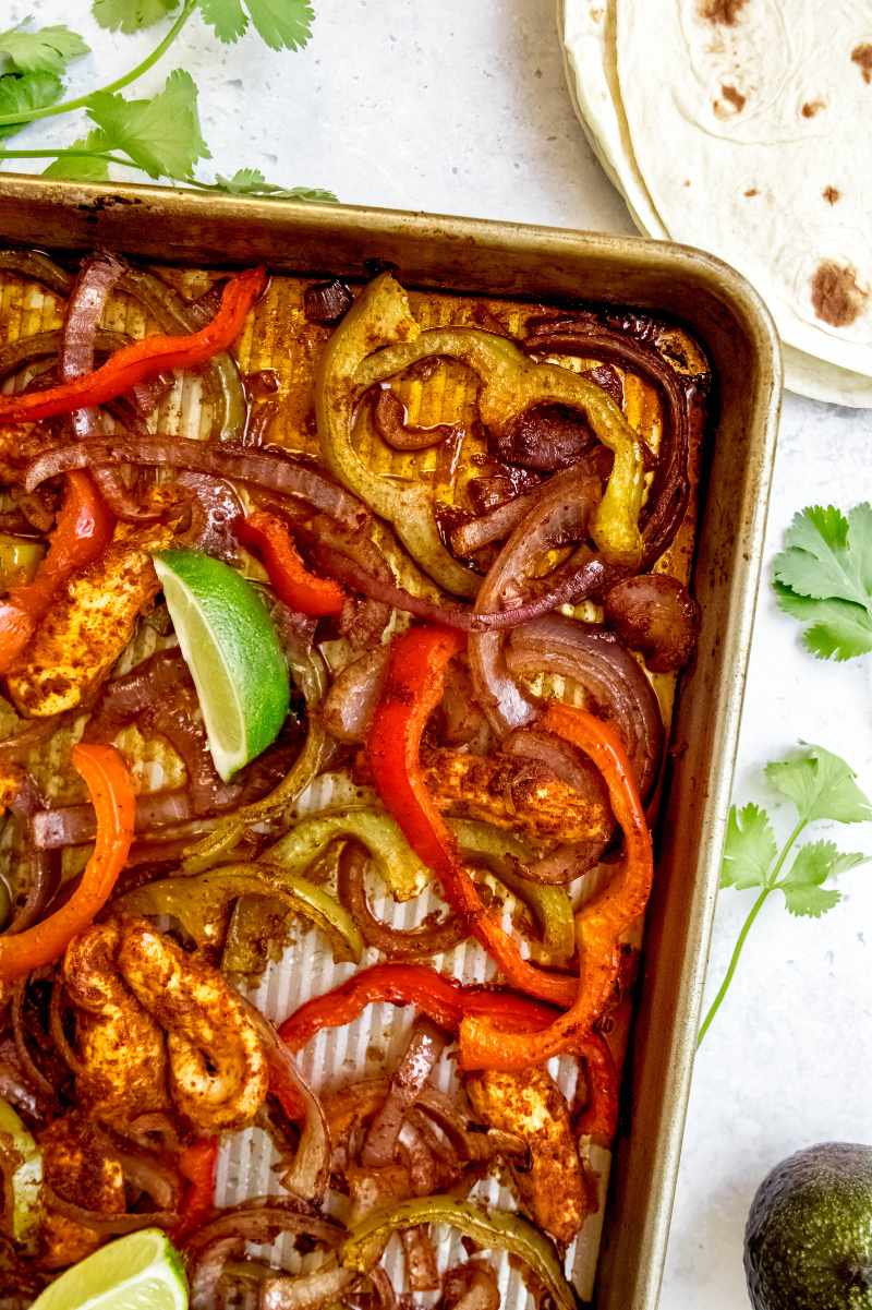 Close view of the corner of a baking sheet with cooked chicken, peppers, and onions