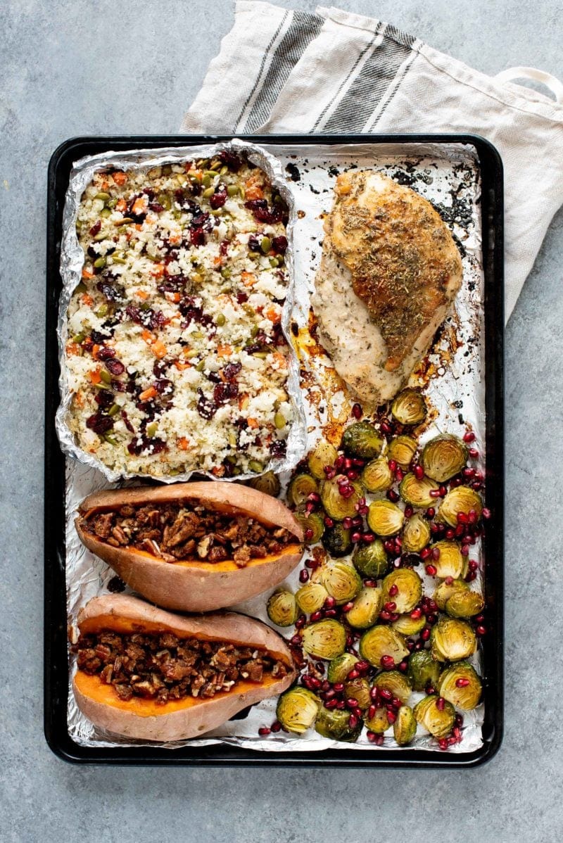 Overhead shot of paleo Thanksgiving dinner cooked on a sheet pan. Components include sweet potatoes, Brussels sprouts, turkey, and cauliflower rice pilaf