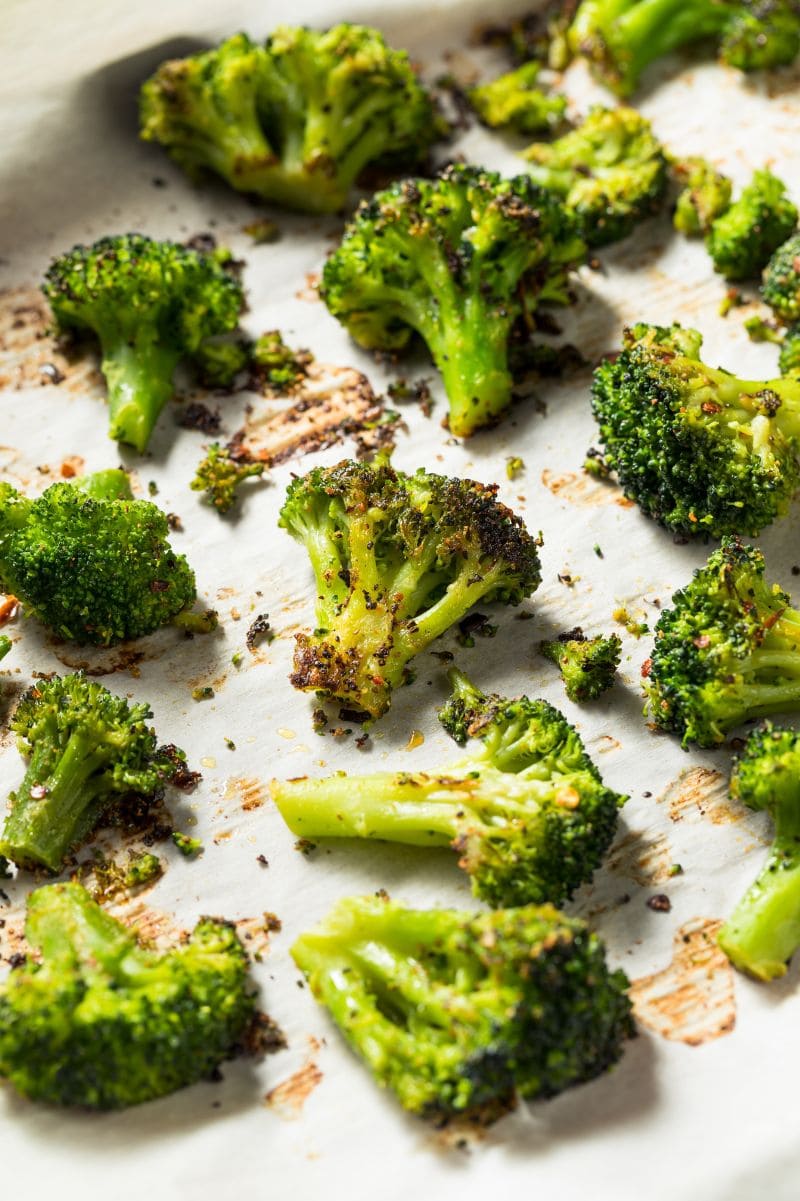 Roasted broccoli on a parchment paper lined sheet pan.