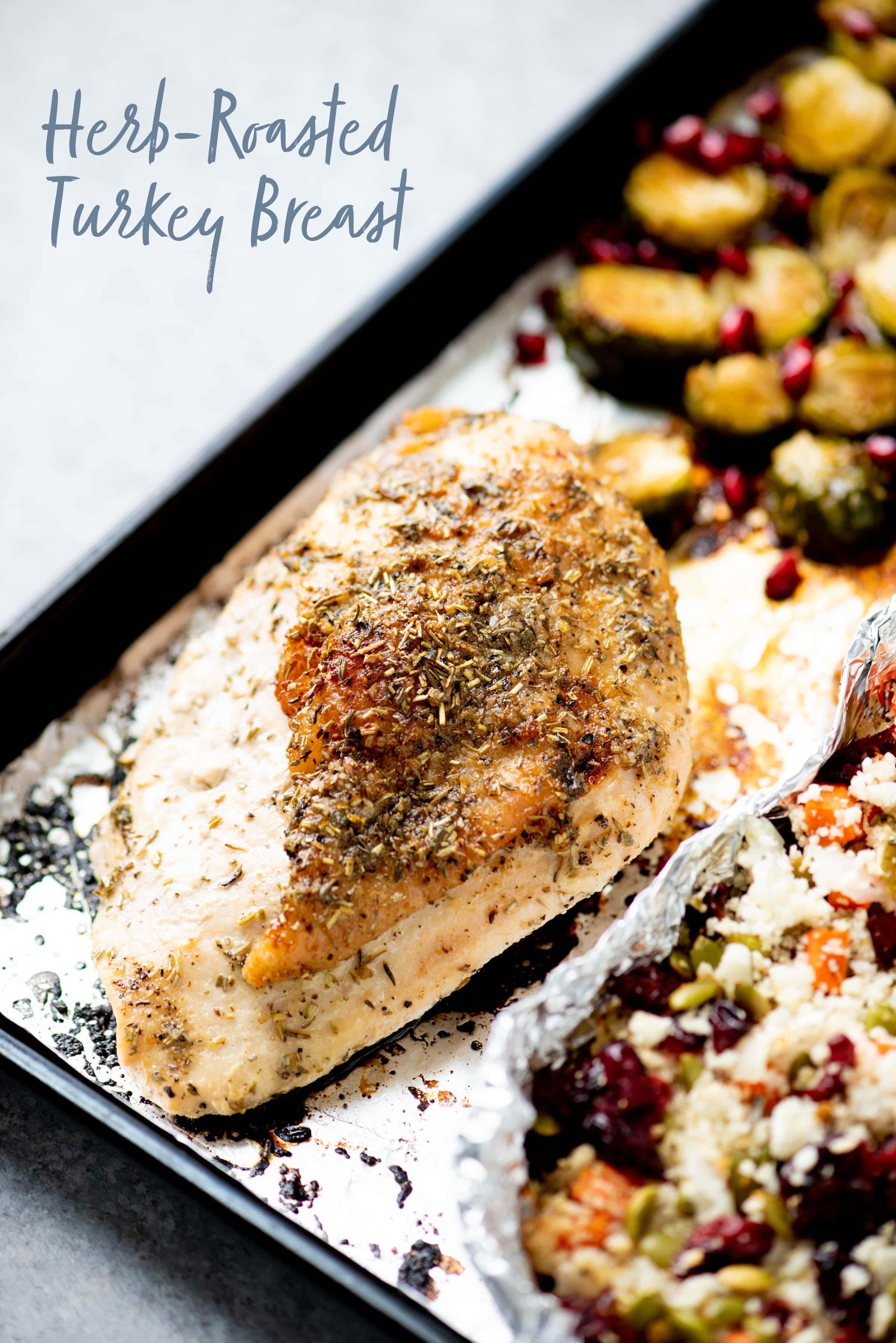 Half a roasted turkey breast on a sheet pan lined with foil. Text overlay reads "herb-roasted turkey breast."