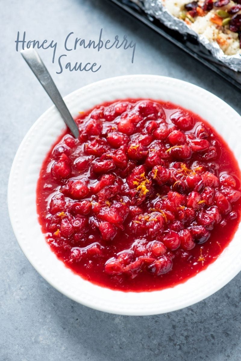 Cranberry sauce in a white bowl with a spoon. Text overlay reads "honey cranberry sauce."