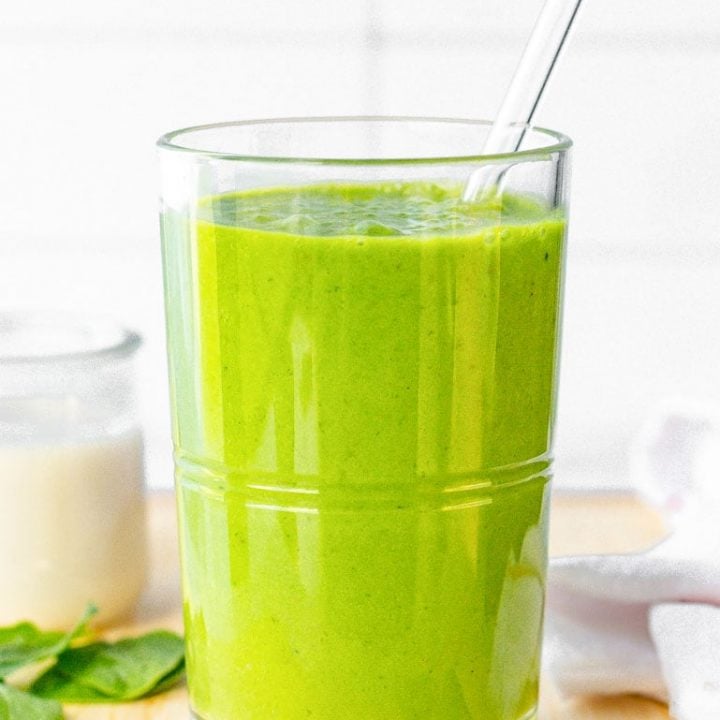 Green smoothie close up on a cutting board with a glass straw in it.