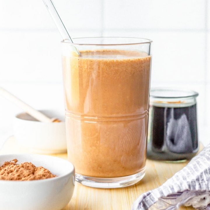 Chocolate coffee smoothie with glass straw on cutting board with ingredients.