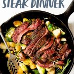 Overhead shot of potatoes and Brussels sprouts in a cast iron skillet, topped with a sliced seared steak