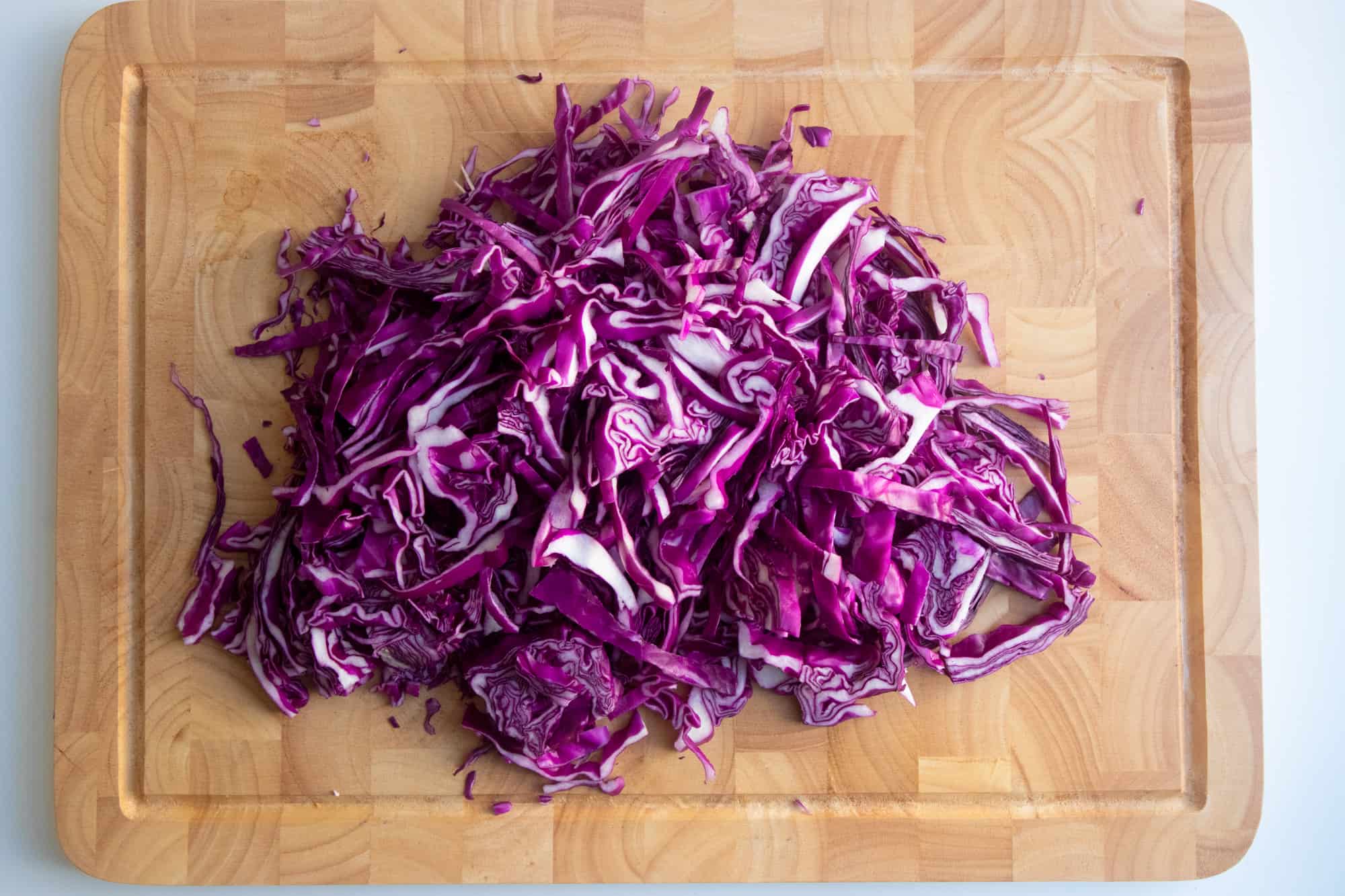 Sliced red cabbage rests on a wooden cutting board.