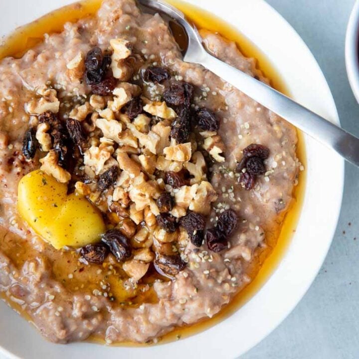 Close view of a bowl of slow cooker breakfast oats garnished with butter, maple syrup, dried fruit, and nuts.