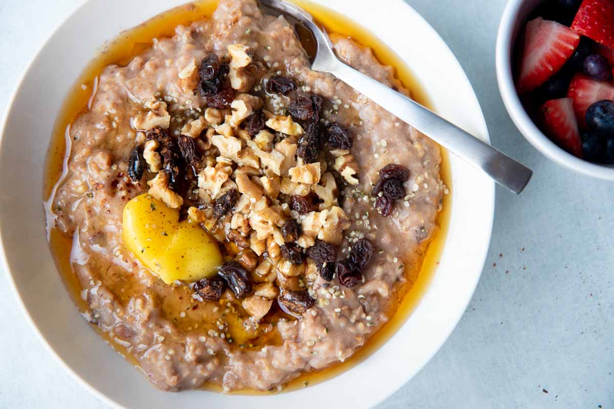 Close view of a bowl of slow cooker breakfast oats garnished with butter, maple syrup, dried fruit, and nuts.