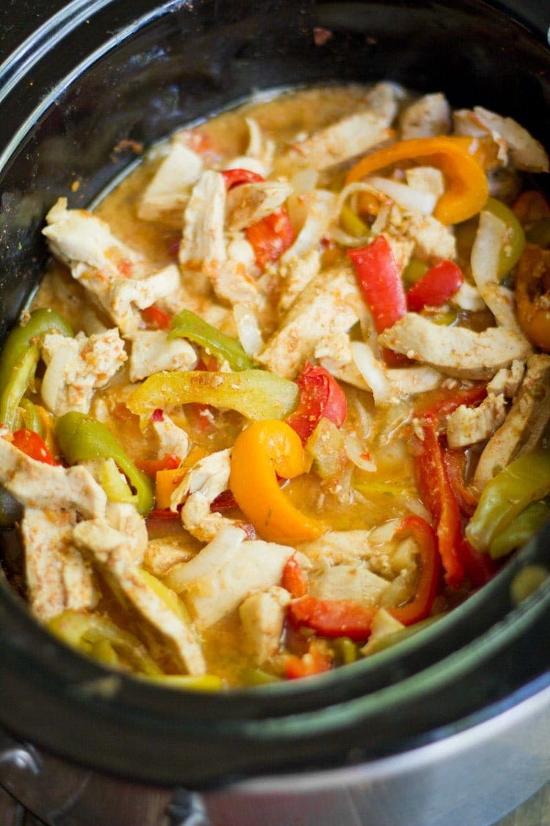 Fajita ingredients cook together inside a crock pot - peppers, chicken and seasonings.