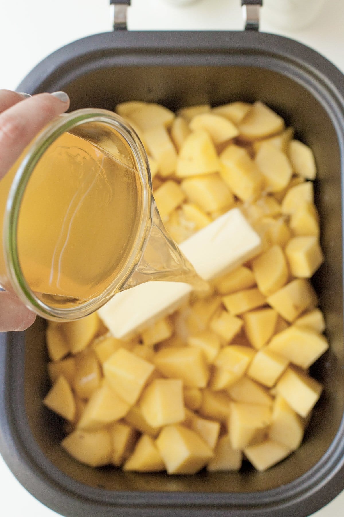 Pouring chicken broth over potatoes and butter in a slow cooker.