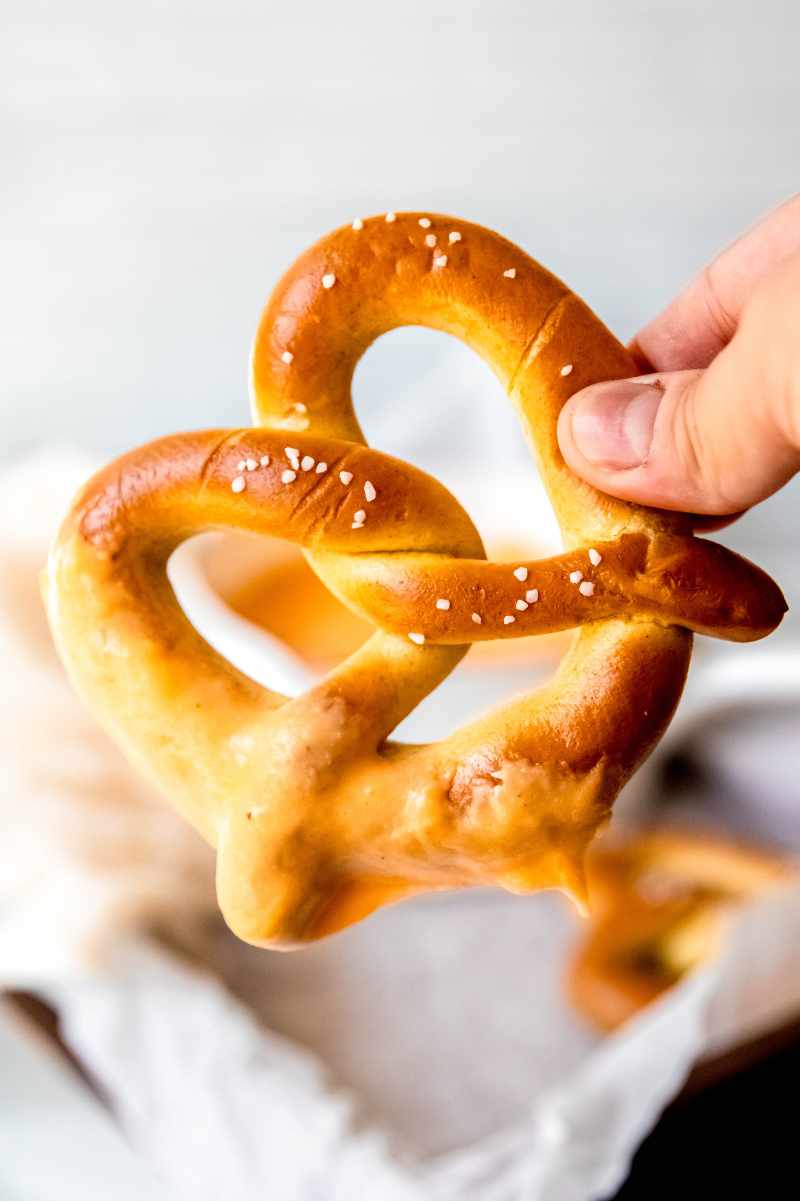 A hand holds up a soft pretzels that has been dunked in creamy cheese dip.