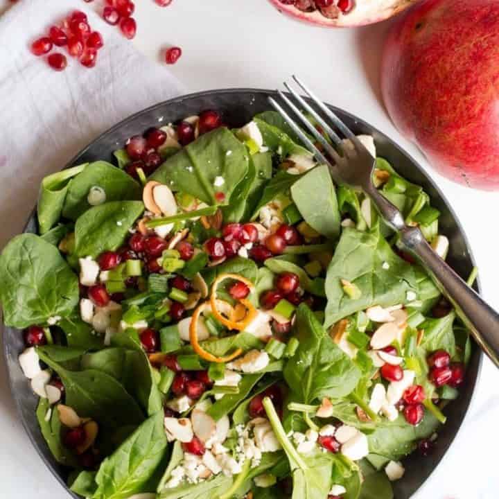 Overhead of spinach and pomegranate salad in a bowl with a split pomegranate alongside.