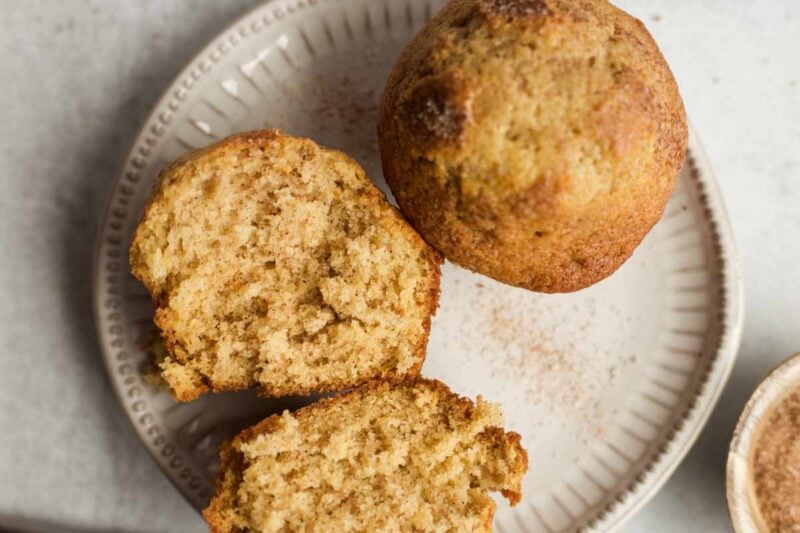 Close view of a split muffin on a plate beside another muffin.