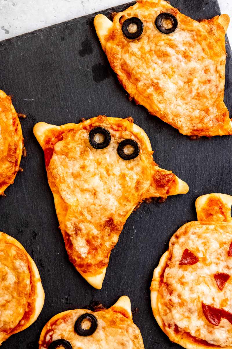 Serving adorably spooky ghost shaped pizzas with black olive circles for eyes on a slate board.