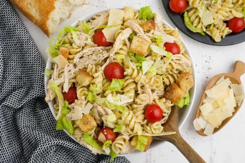 Top view of a wooden spoon tucked into a bowl of pasta with bread and shaved parmesan alongside.