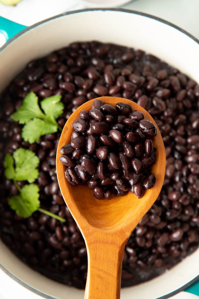 A wooden spoon full of cooked beans held above the pot of finished beans.