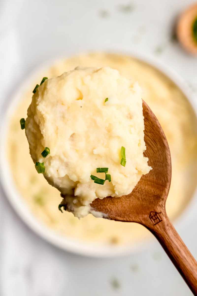 Close view of a wooden spoon holding up a big scoop of Instant Pot mashed potatoes.