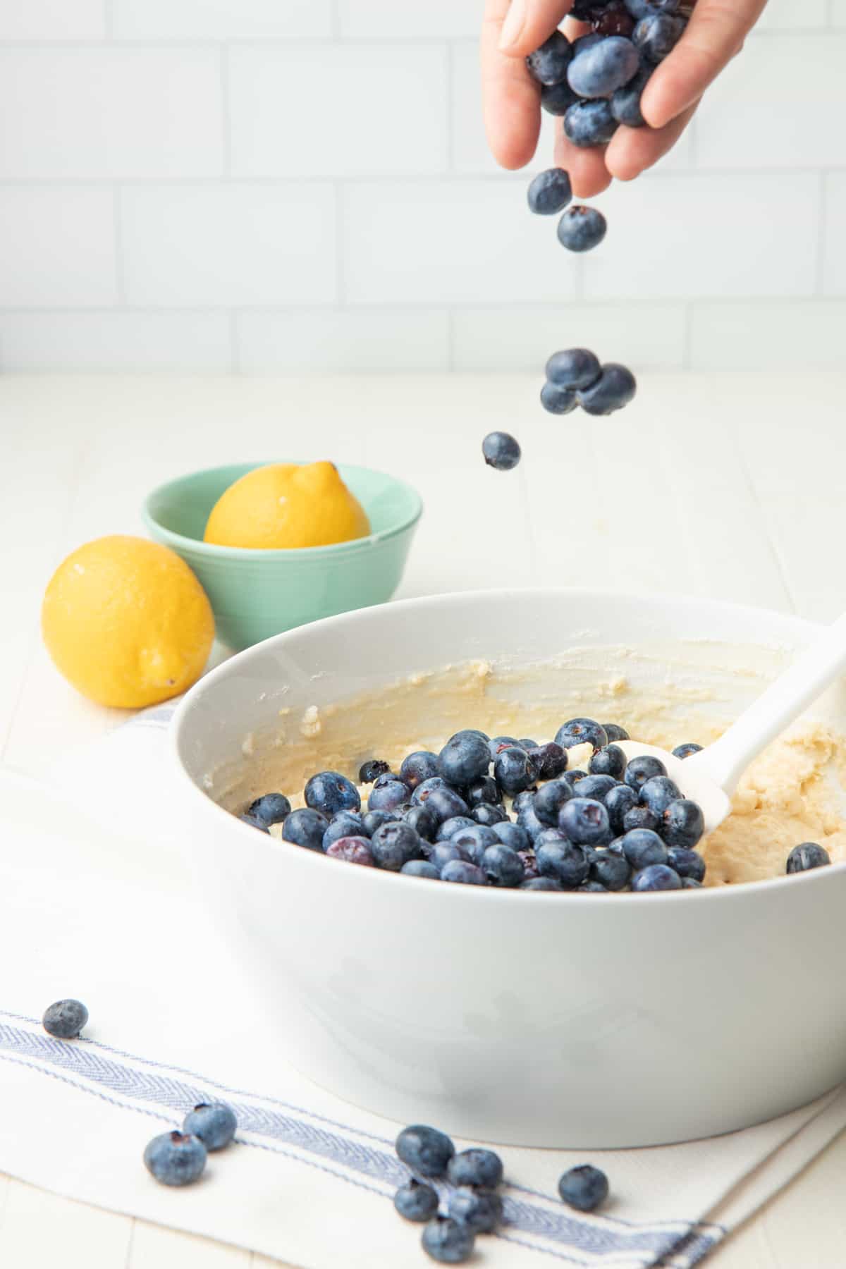 A hand sprinkles blueberries into a muffin batter.