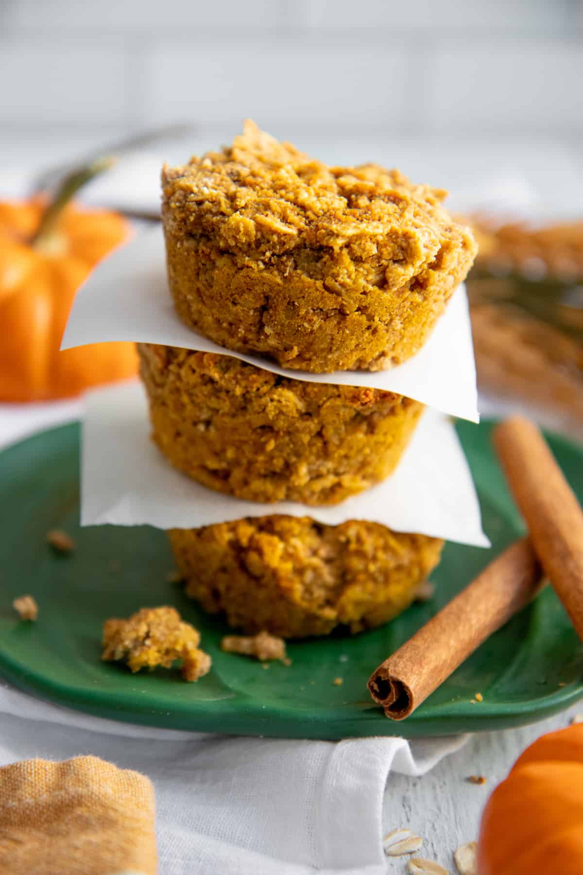 Three Pumpkin Spice Baked Oatmeal Cups stacked on a green plate, with pieces of parchment paper separating them