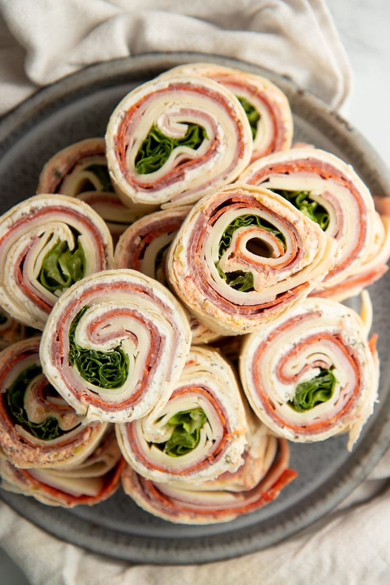 Top view of pinwheel roll-ups stacked on a platter showcasing the spirals of fillings.