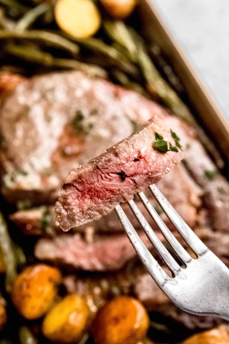 A fork holds up a bite of perfectly cooked steak.